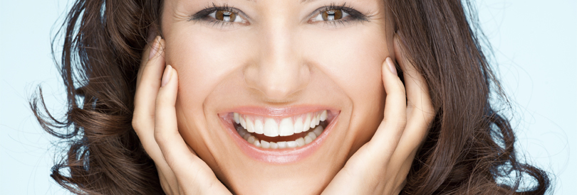 extreme close up of woman's face as she smiles with teeth and holds her face