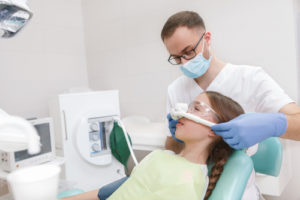 Male dentist putting inhalation sedation mask on a young girl in dental chair,