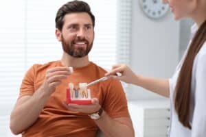 A man pointing to his teeth and holding a model of a dental implant