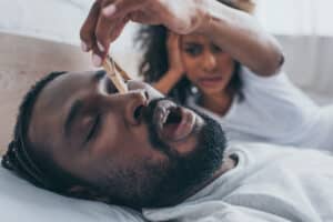 A woman pinching her husband's nose with a clothespin while he snores