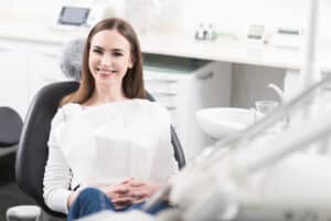 A woman sitting in a dentist's chair and smiling after a 3D facial scan in Melville, NY