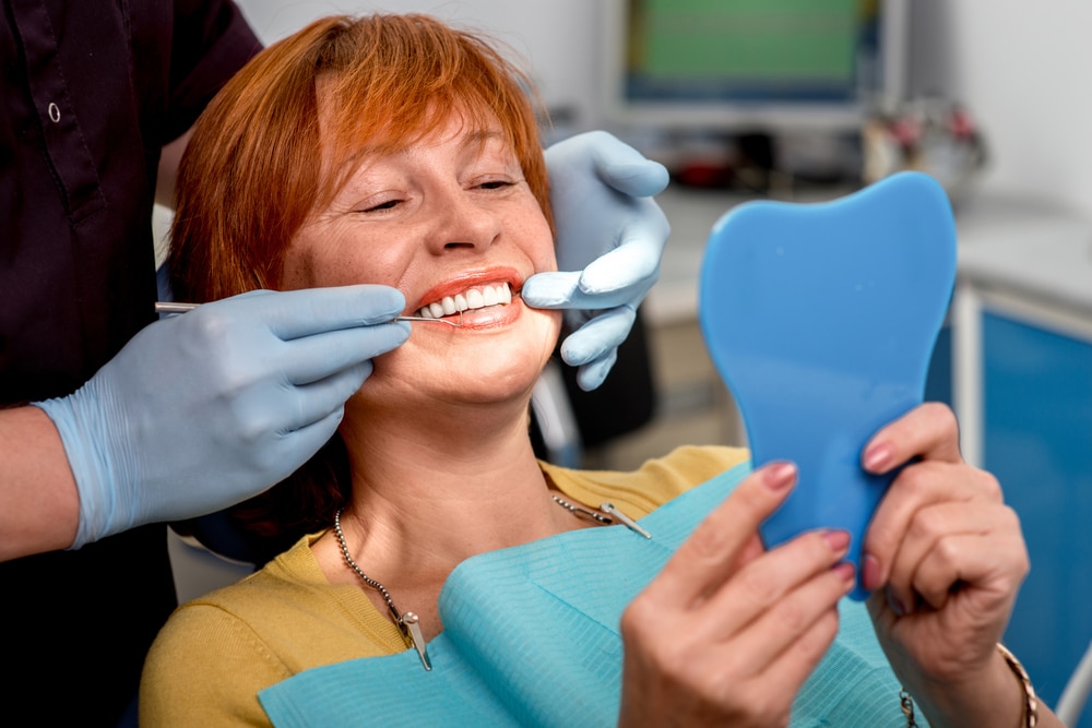A woman looking in the mirror after getting dental implants in Melville, NY